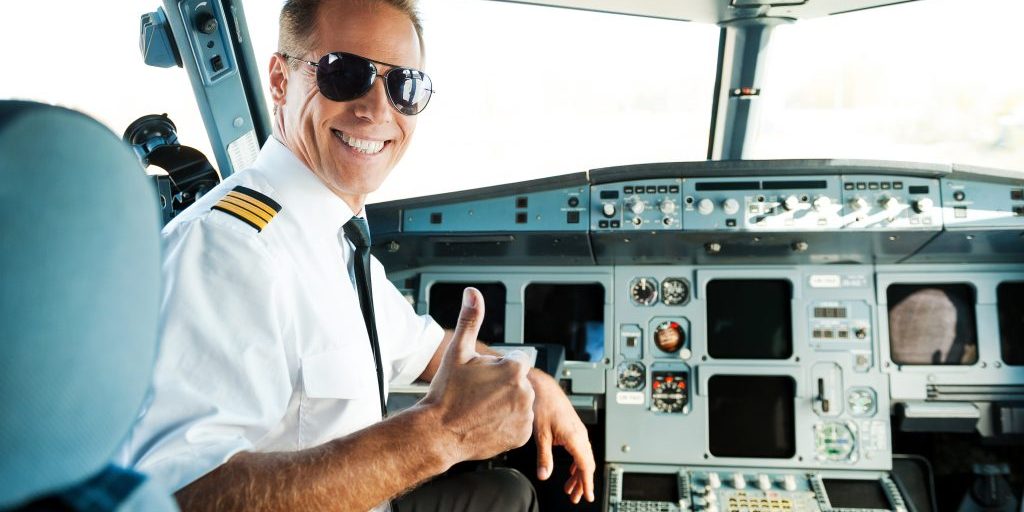 Rear view of confident male pilot showing his thumb up and smiling while sitting in cockpit